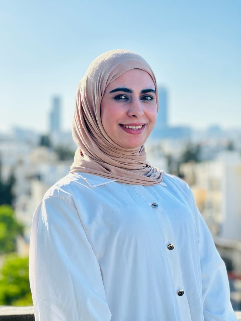 A portrait of Teacher Muradi Al-Hawari with a bright smile, against the Amman, Jordan skyline in the background.