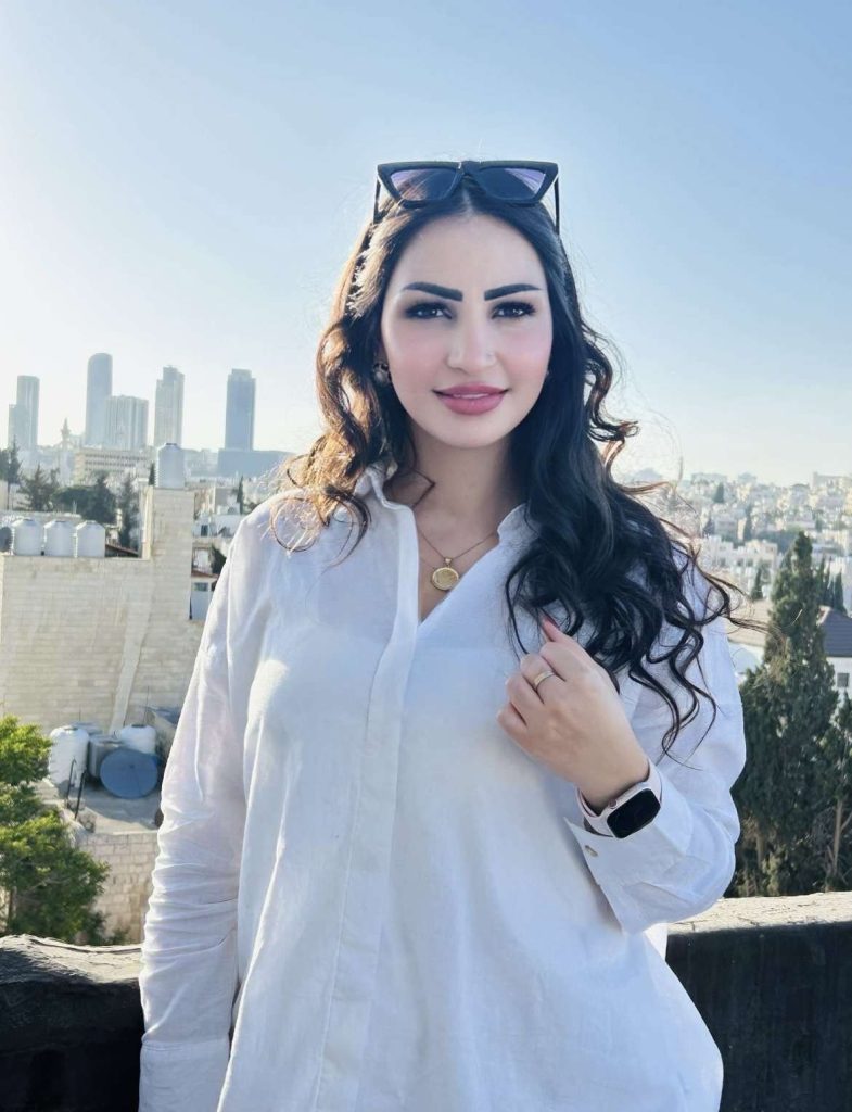 A portrait of Teacher Aya Al-Masry smiling, with the Amman, Jordan skyline in the background.