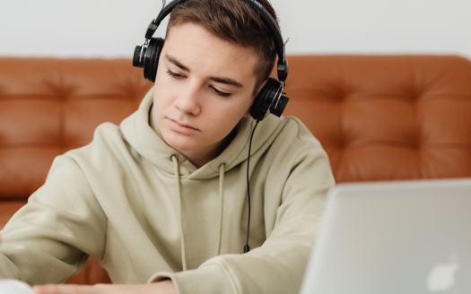 A student studying online using headphones and a laptop for a remote Arabic language course.